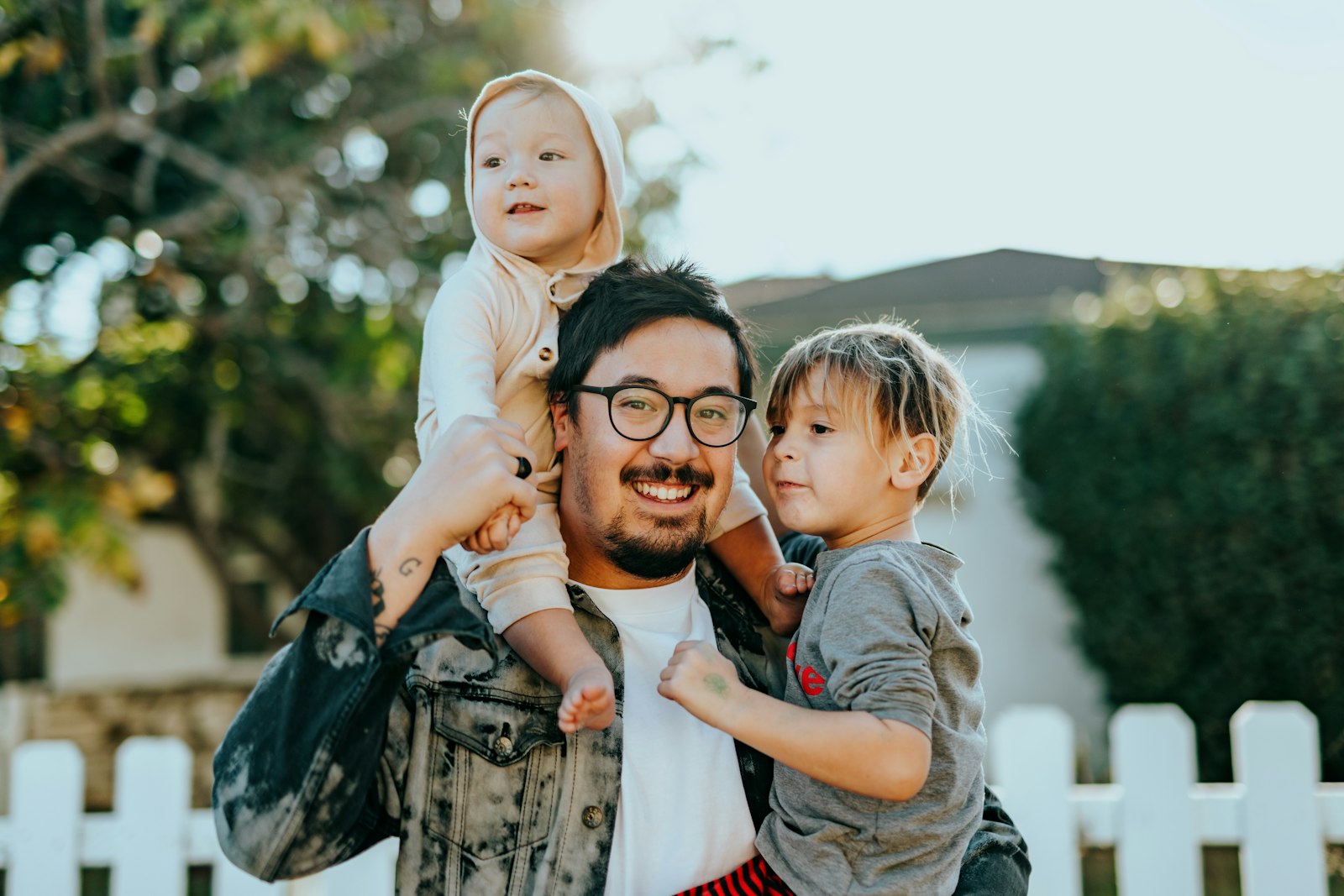 A dad laughing with his two kids in front of their home